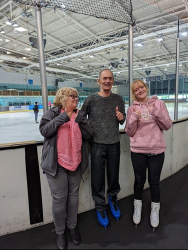 Man ice skates supported by 2 Care Assistants